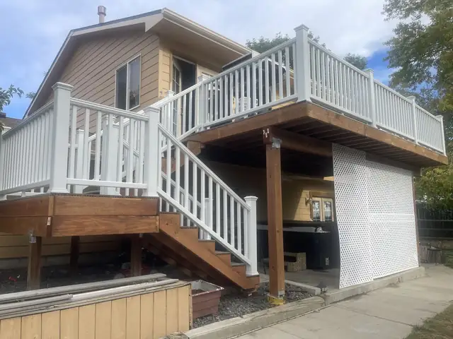 Raised wood deck with white railings and stairs over a patio, with lattice screening below