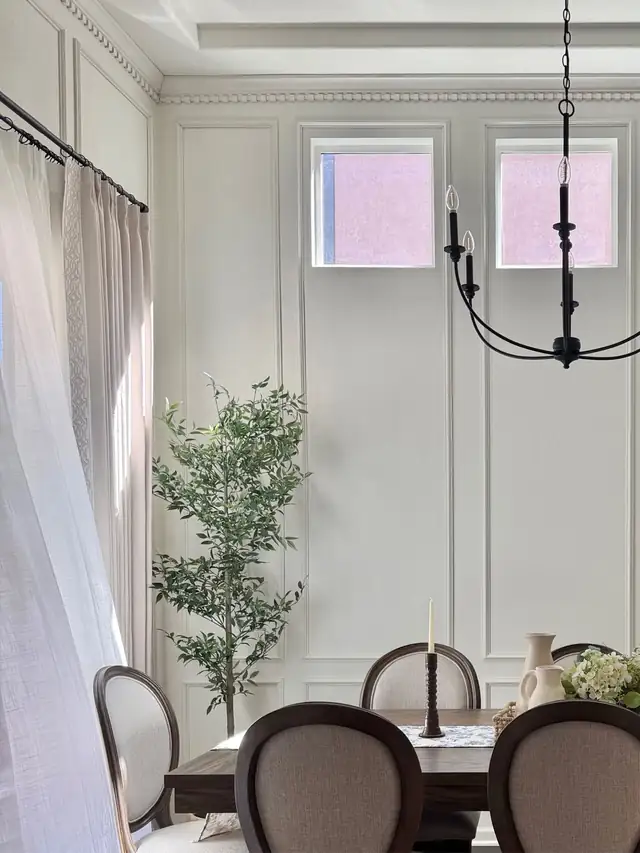 Tall dining room wall with white board and batten molding, a chandelier and a potted tree