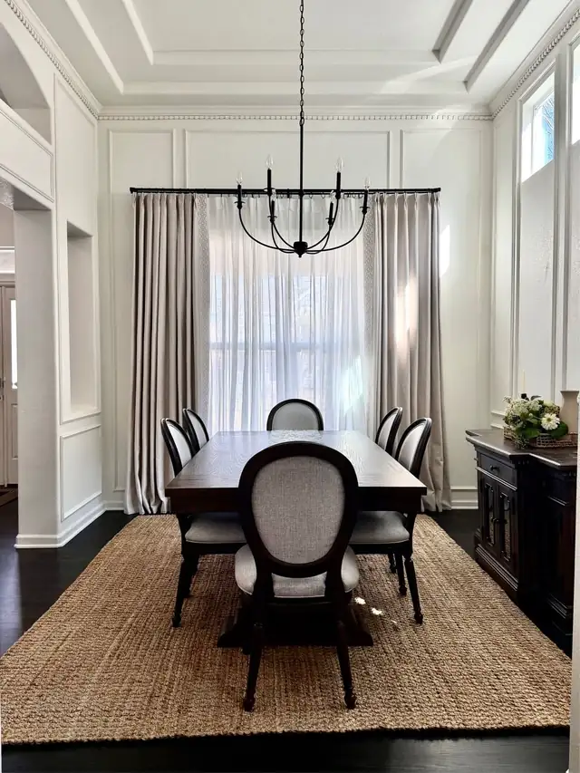 Formal dining room with white wall molding panels, tall drapes, a long wood table and an iron chandelier