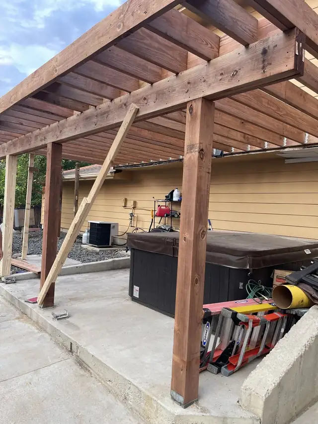 New wood posts and beams going in under a raised deck above a patio and hot tub